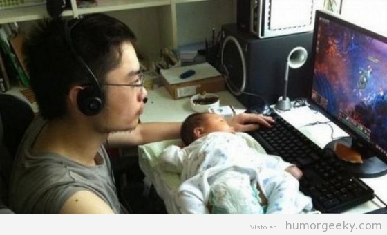 Padre jugando al ordenador con bebé encima de la mesa